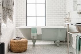 A bathroom with a clawfoot bathtub a wicker stool and towels hanging and folded on fixtures