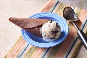 Ice cream cone on a plate next to a scoop on a striped cloth