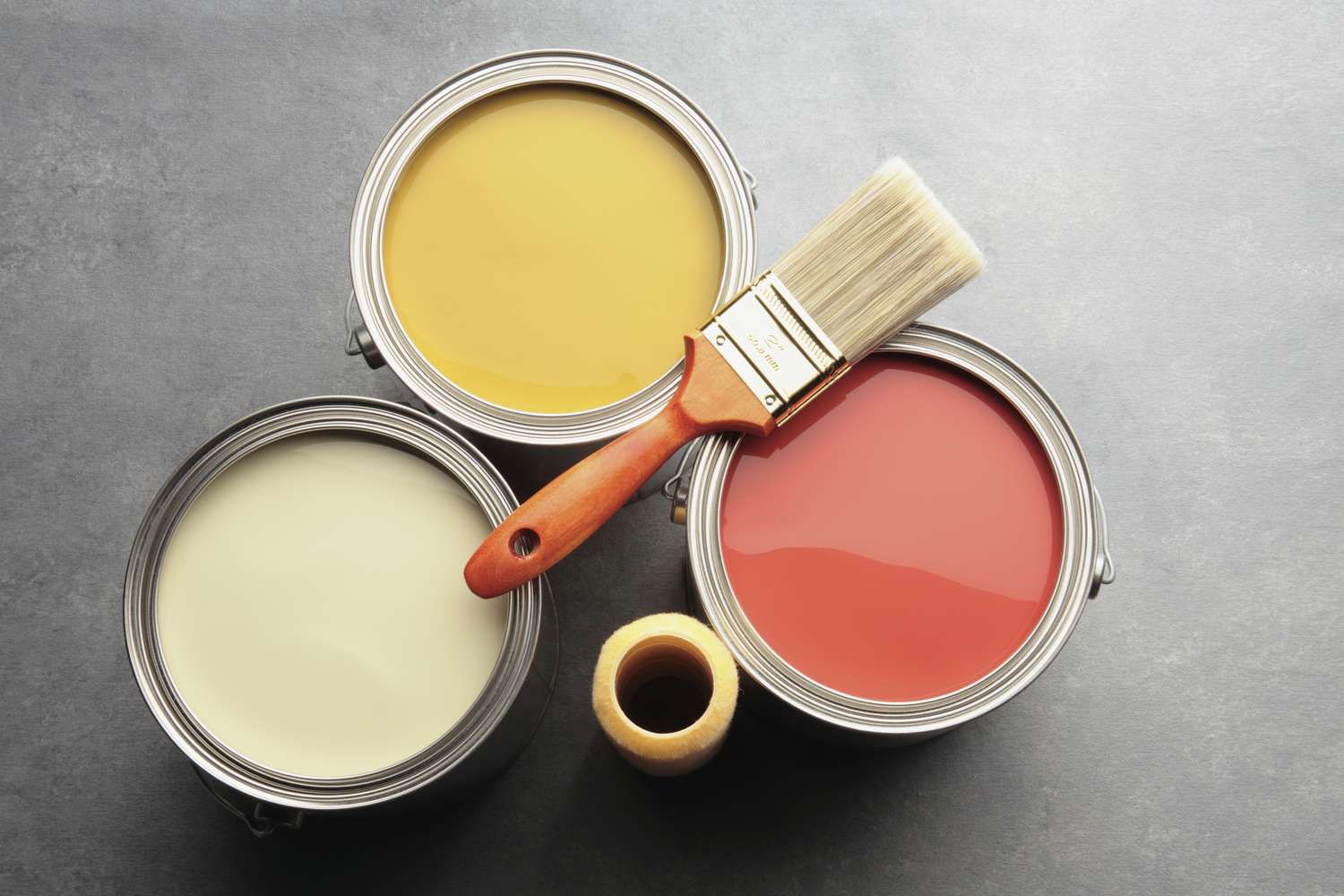 Three open paint cans with a brush arranged on a flat surface