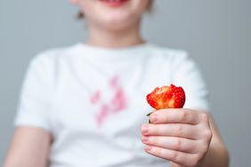 Child's hand holding a sliced strawberry and stained white t-shirt