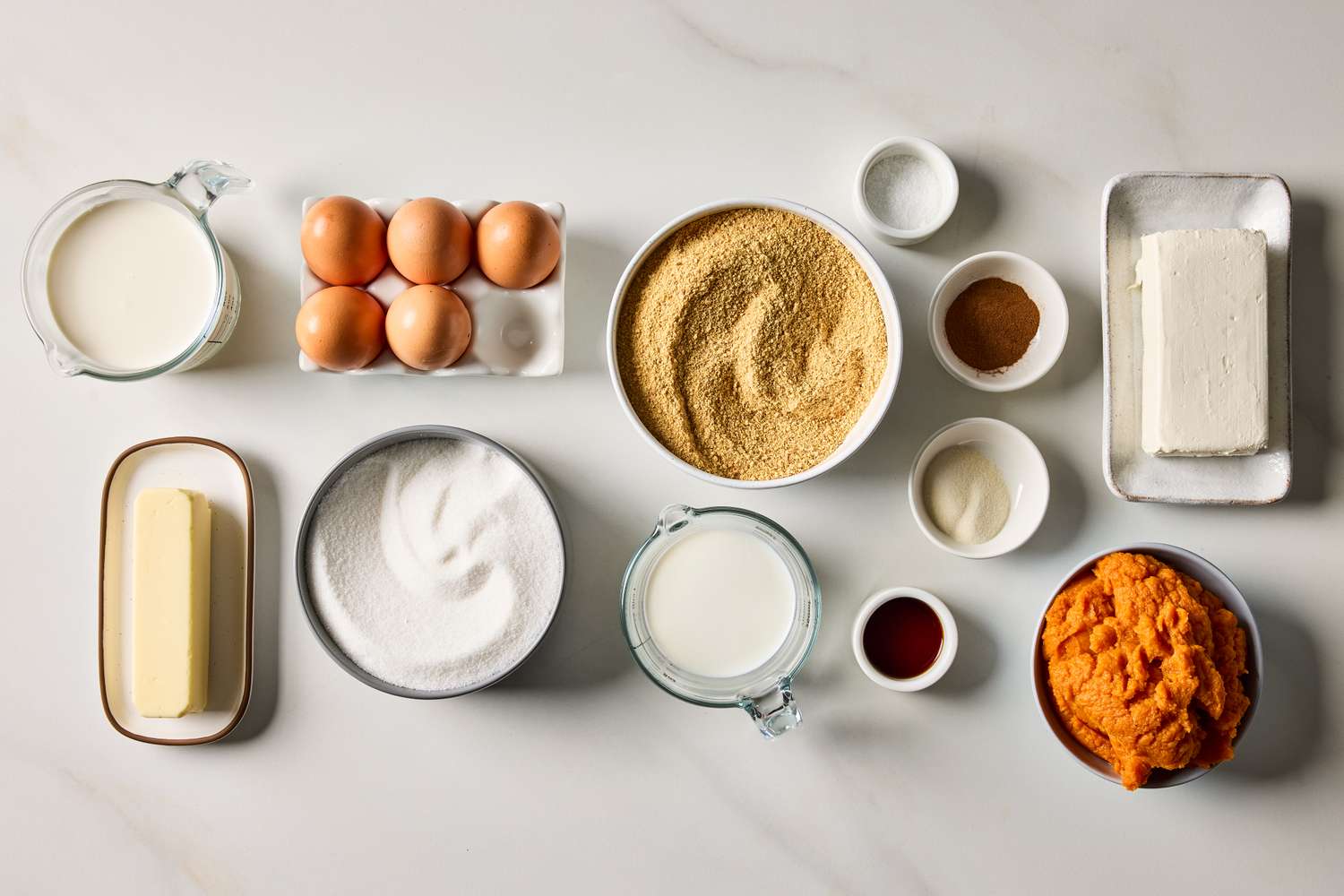Ingredients for making a pumpkin mousse cheesecake arranged on a white surface