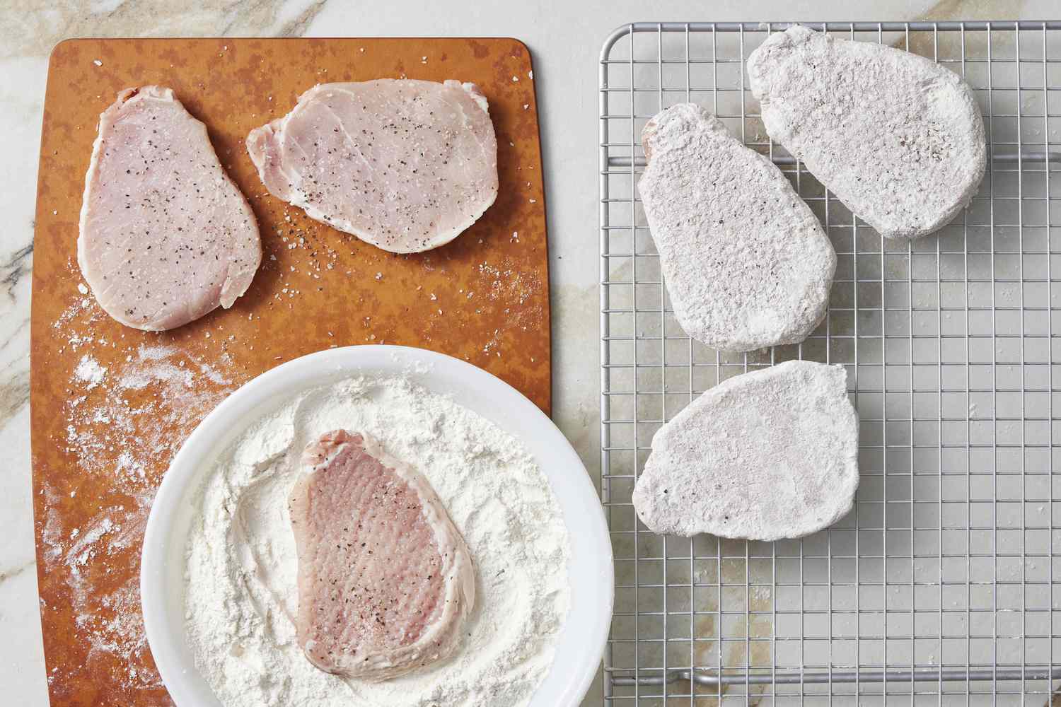 Pork on metal rack dredged in flour, raw pork on cutting board