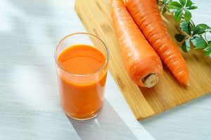glass of carrot juice and chopping board with carrots