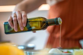 A person pouring olive oil onto food in a kitchen