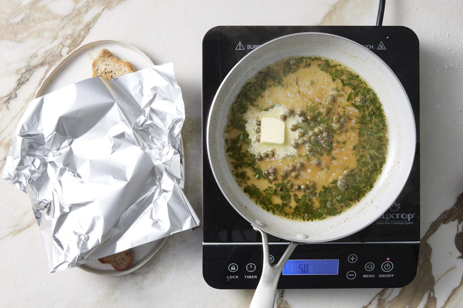 Butter being added to pan with oil, herbs and capers