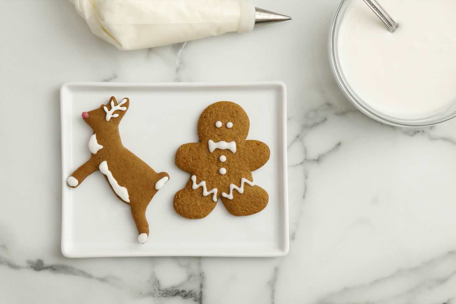 overhead view of two gingerbread cookies and frosting bowl