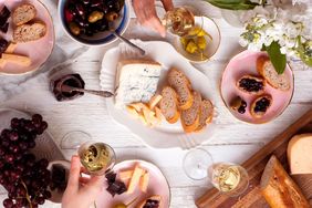 Table set for a dinner party with assorted foods such as bread cheeses and fruits along with glasses of wine