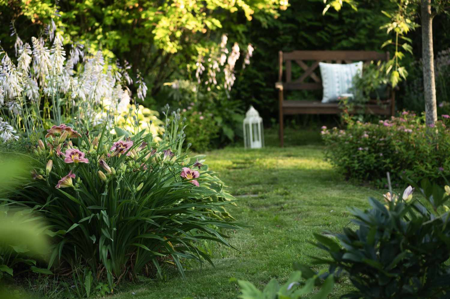 A garden scene with flowers grass a bench and a lantern