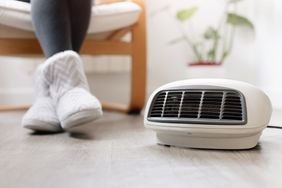 A person wearing slippers sitting near a portable space heater on the floor indoors
