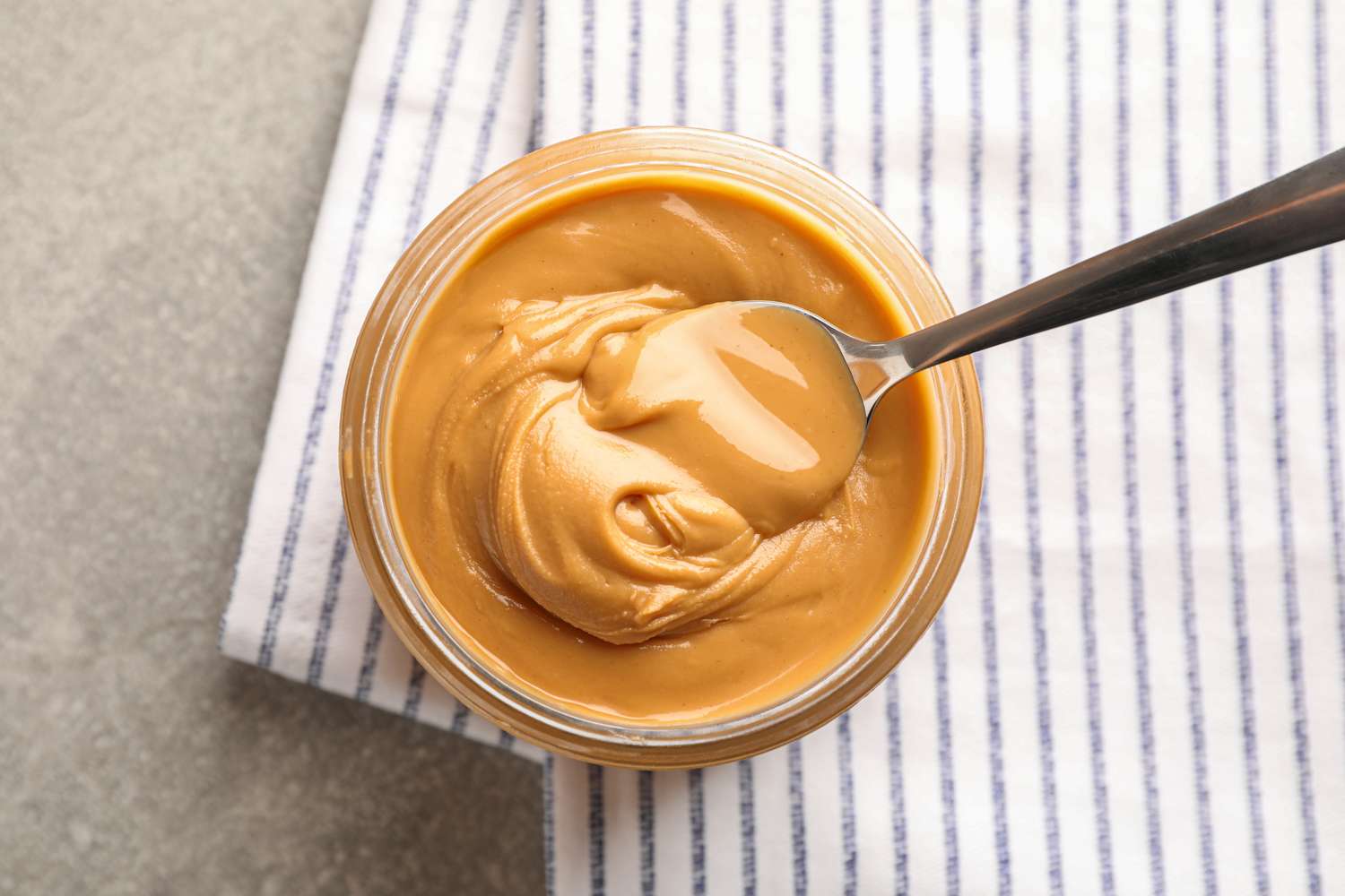 A jar of peanut butter with a spoon resting inside placed on a striped napkin