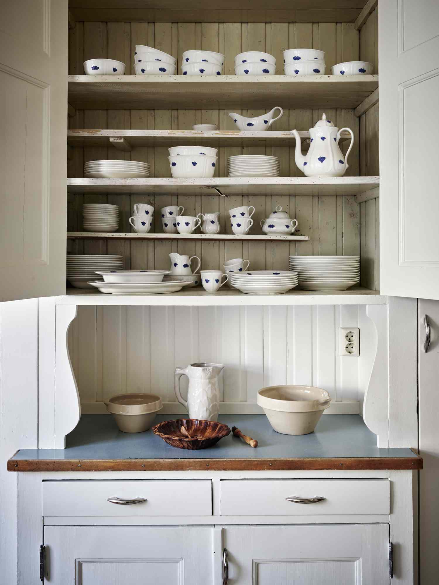 Open kitchen cabinet showcasing neatly arranged dishes and cups on shelves with a light blue countertop below