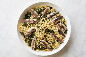 A plate of pasta topped with sardines and sauted greens highlighting a seafood pasta dish