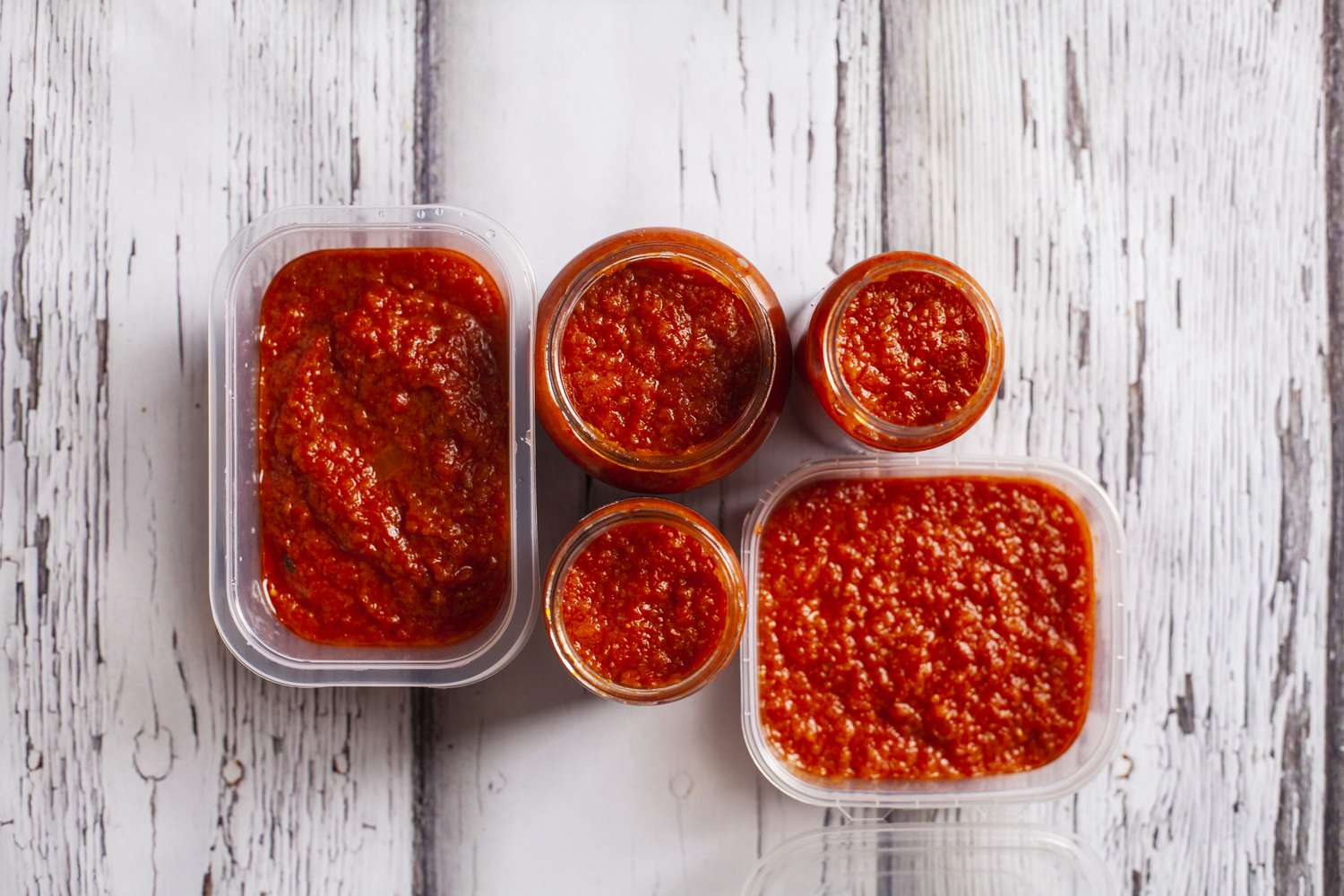 Containers filled with homemade fried tomato sauce, for preserves. On white wooden background. 