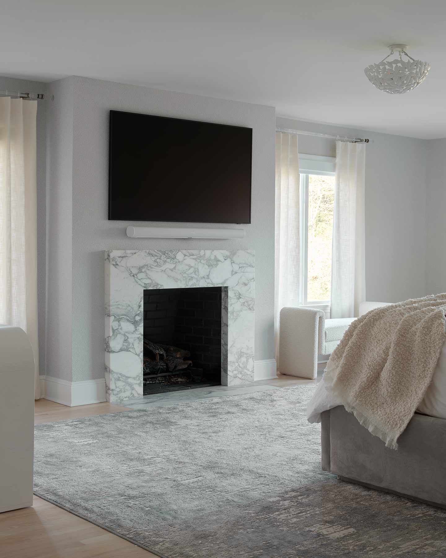 A minimal gray and white primary bedroom with a fireplace that has a marble surround and a gray and white mixed rug underneath.