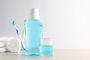 Mouthwash bottle and glass on a countertop toothbrush and dental floss in the background