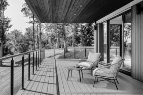 A modern outdoor deck with seating glass railings and forest views