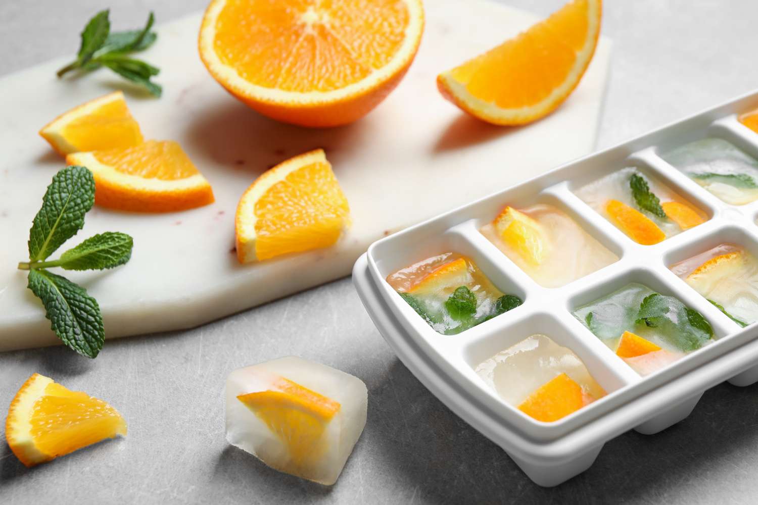 Ice cube tray with citrus slices and mint orange wedges on a marble surface