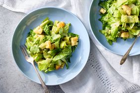 Two plates of Caesar salad with croutons served on a light surface with forks