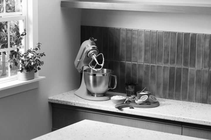 Kitchen counter with a stand mixer ingredients and fruit arranged near a cutting board