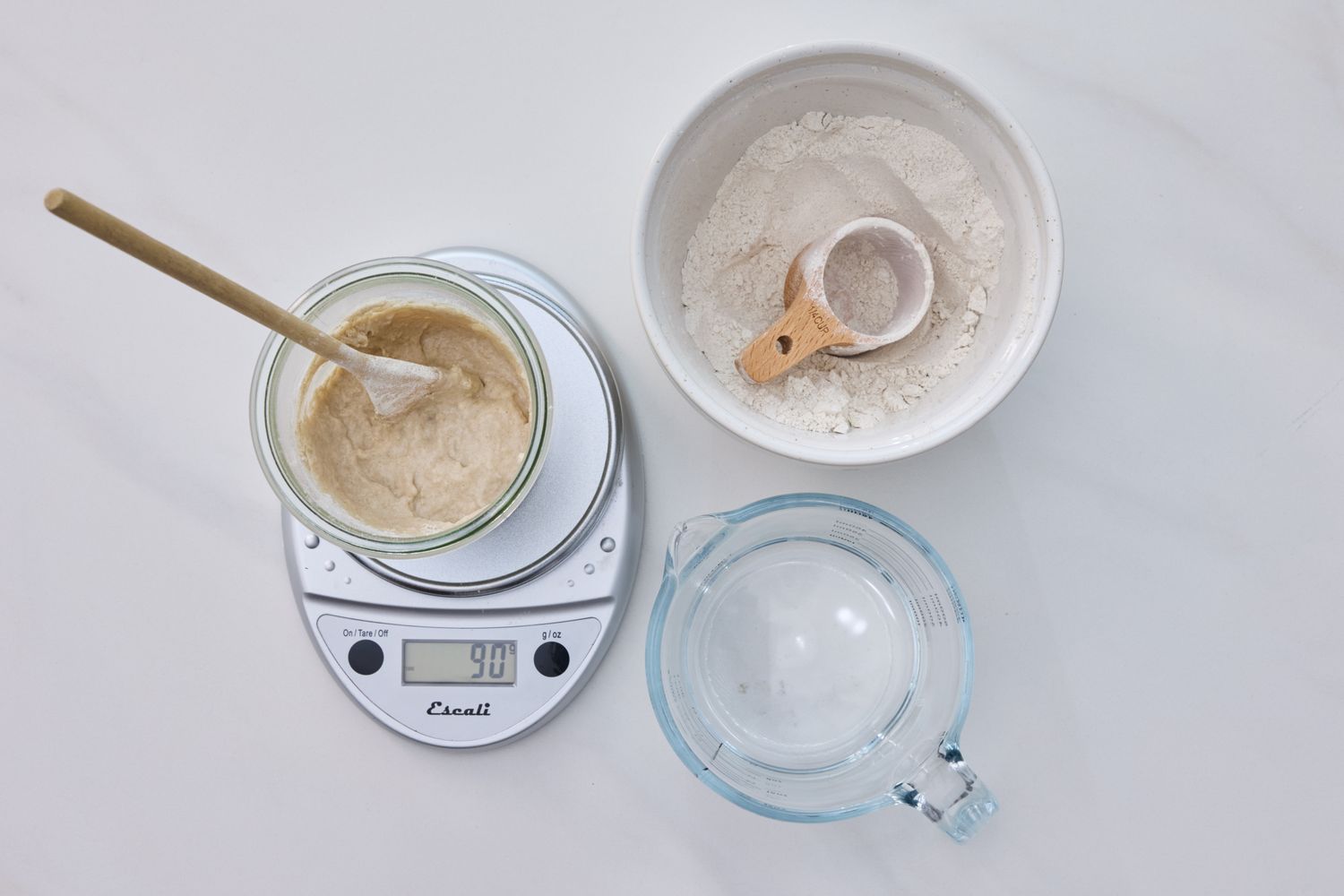 Ingredients and tools for making sourdough starter including a jar on a scale a bowl of flour and a measuring cup