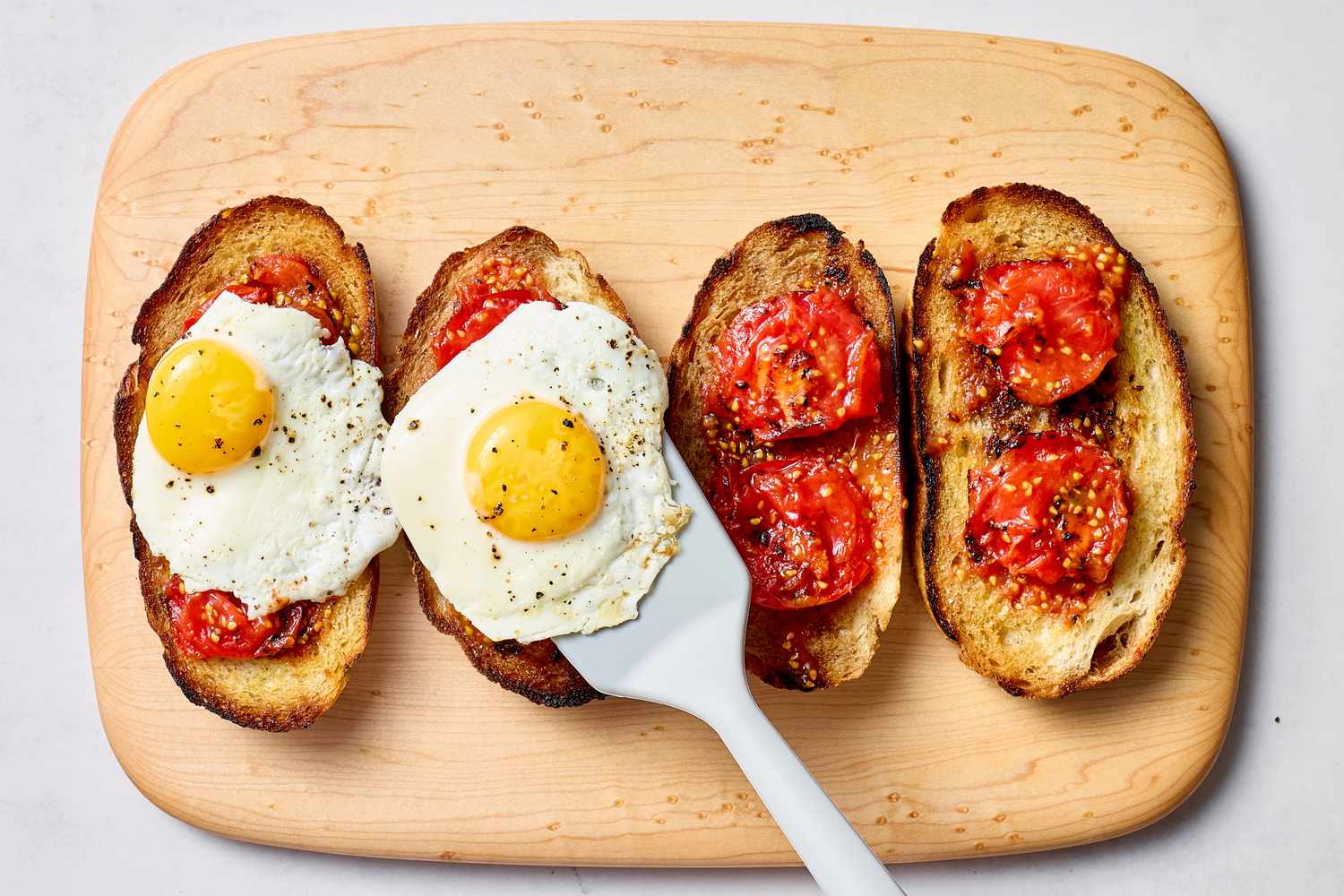 Toasts topped with charred tomatoes and fried eggs on a cutting board