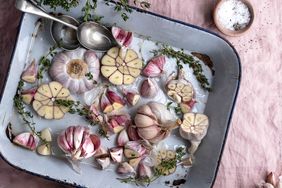 Halved garlic bulbs and sprigs of thyme in a baking dish with spoons on the side