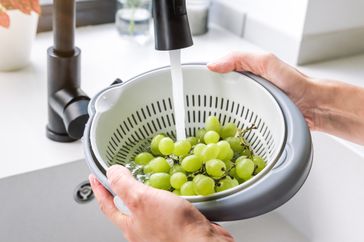 Someone washing grapes in a colander under a faucet
