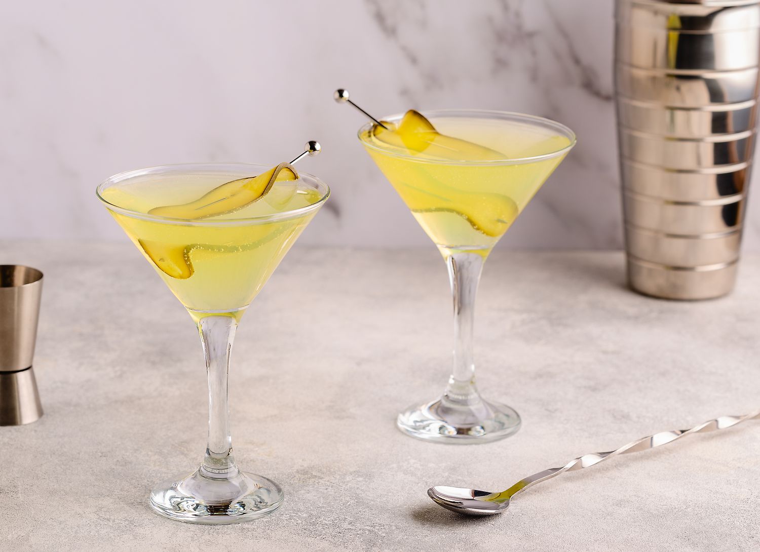 two pickle martinis with a shaker and spoon