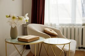 A cozy living space featuring a chair with a pillow a vase of flowers and two small tables with a book and glass tops