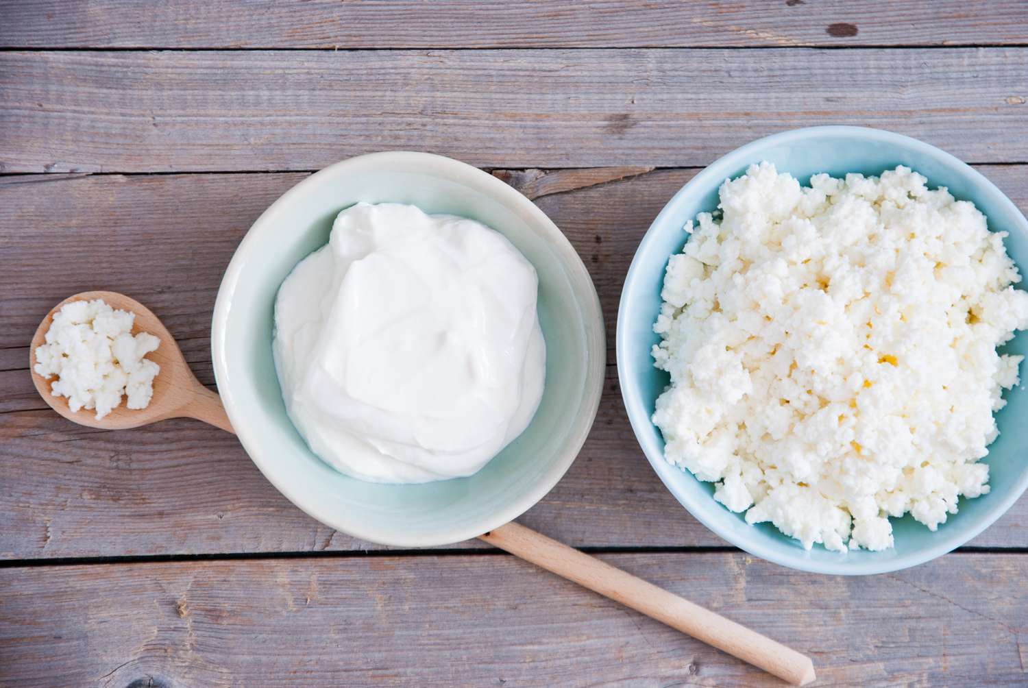bowl of yogurt and a bowl and a spoon of cottage cheese on pale wood surface