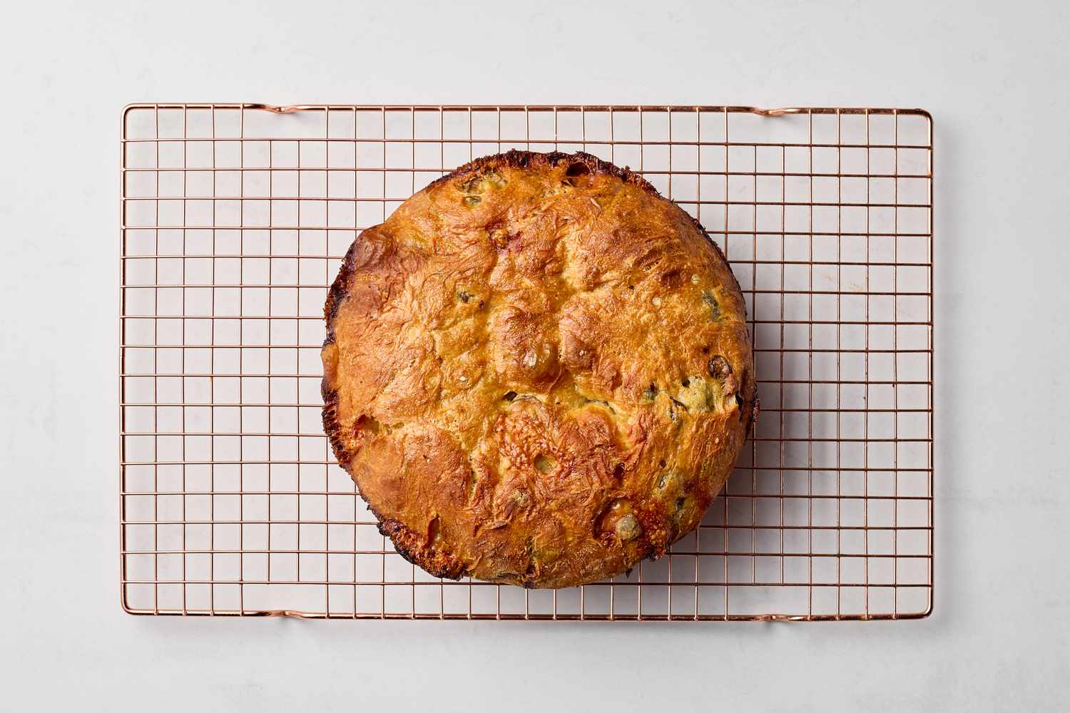 A loaf of bread with olives and cheese on a cooling rack