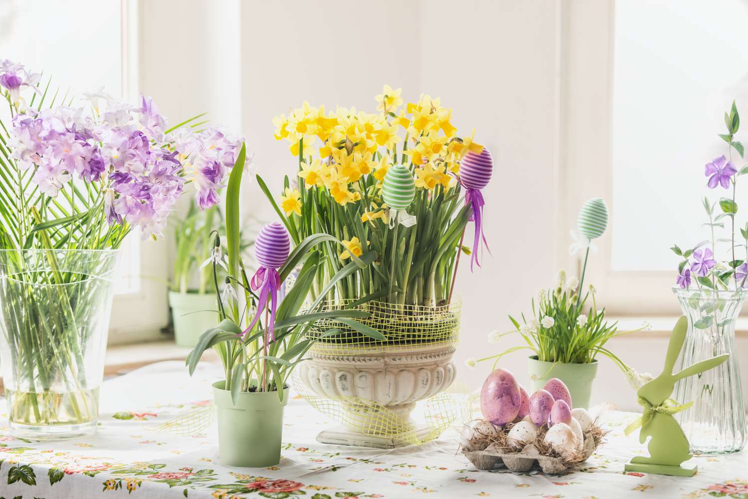 Easter decorations with eggs, rabbits and various springtime flowers in pots and vases, yellow daffodils and purple hyacinths, on table at sunny window.. 
