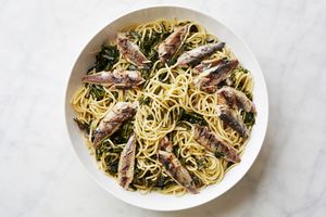 A plate of pasta topped with sardines and sauted greens highlighting a seafood pasta dish