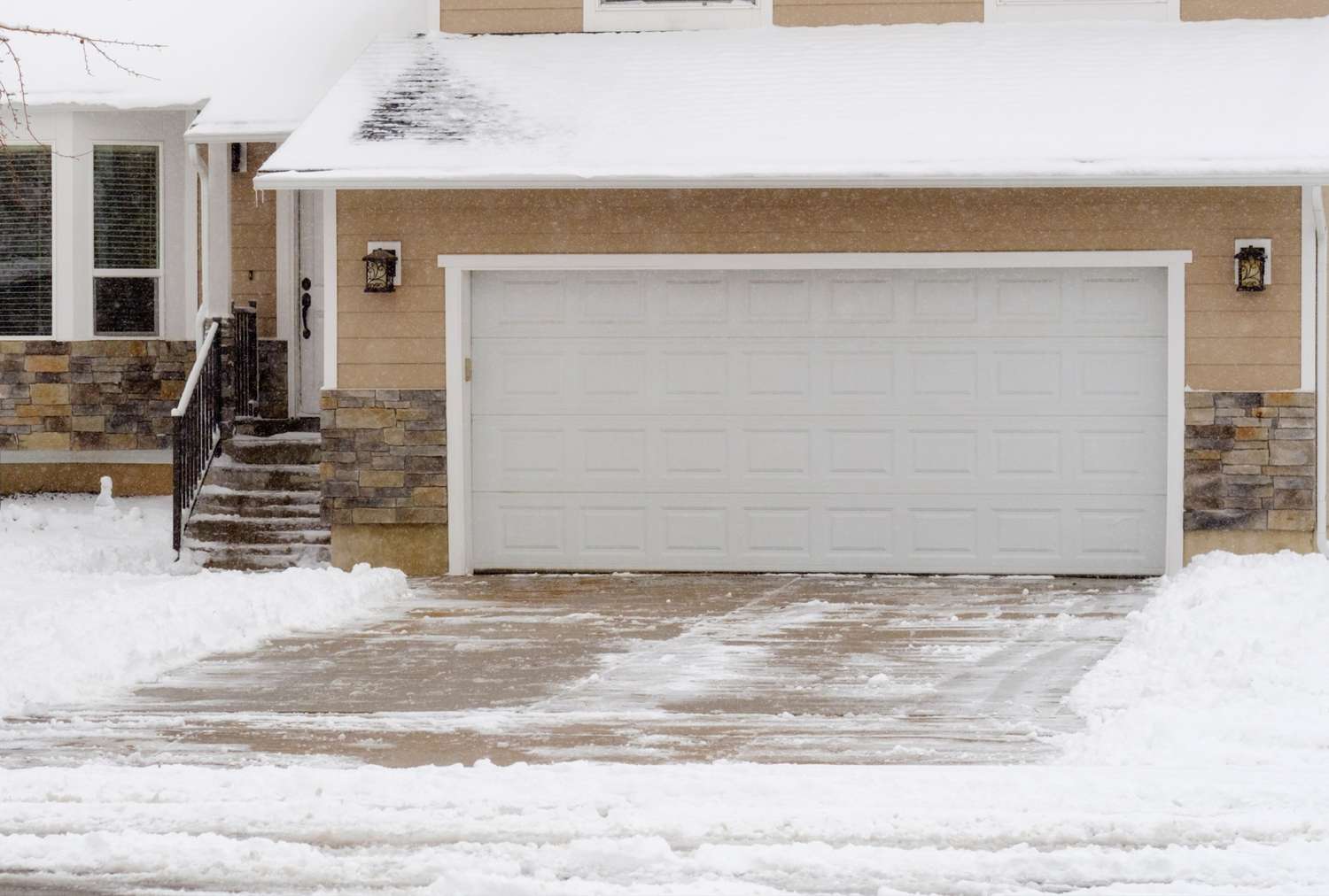 Snowcovered driveway and house exterior with a garage door