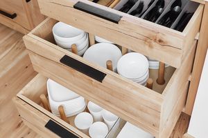 Open wooden kitchen drawers organized with plates bowls cups and utensils