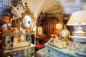 An antique shop display featuring a range of vintage furniture mirrors clocks and decorative items arranged in an ornate style