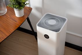 An air purifier placed beside a wooden table with a plant on top