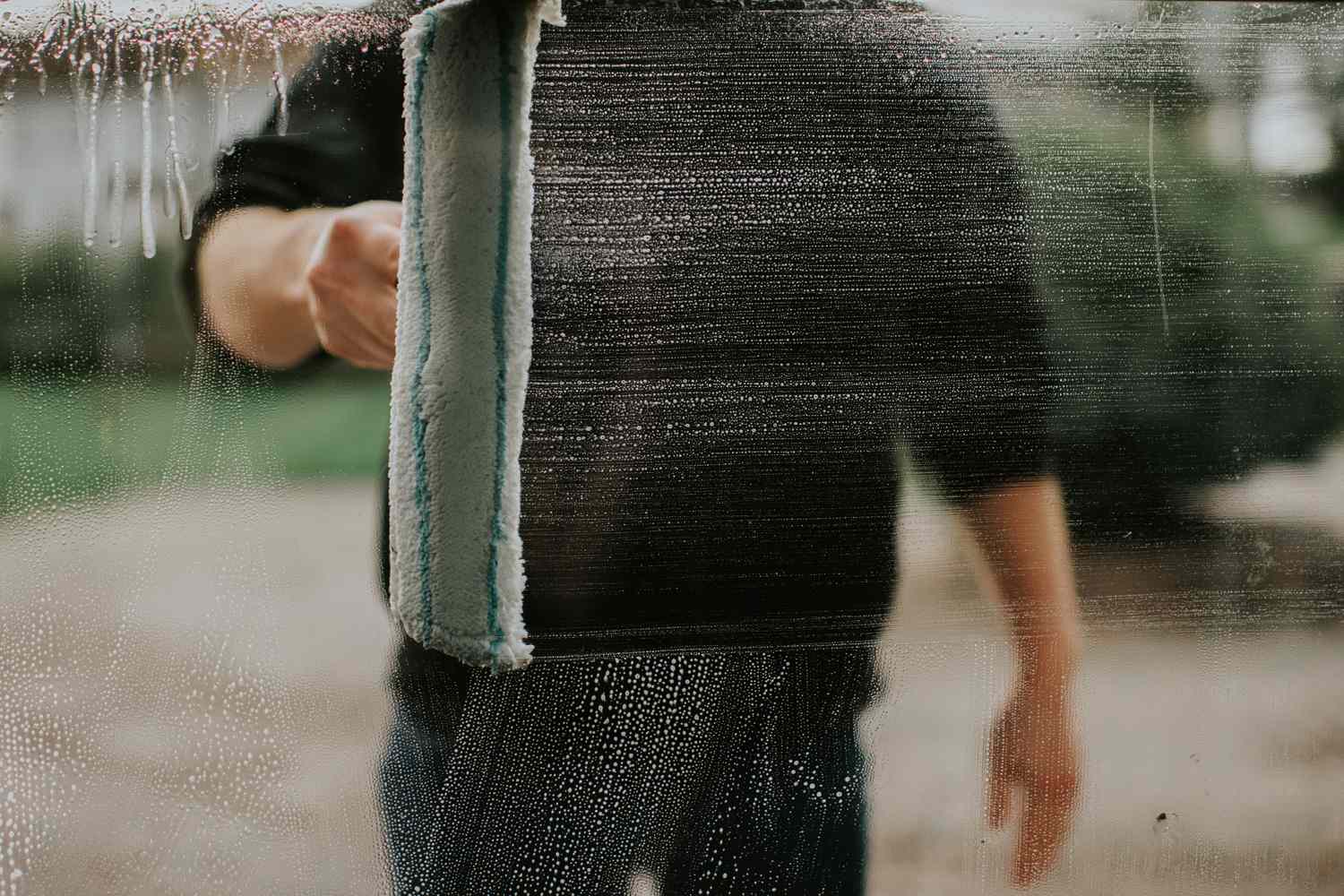 A person cleaning a glass surface with a window squeegee partially removing streaks and water marks