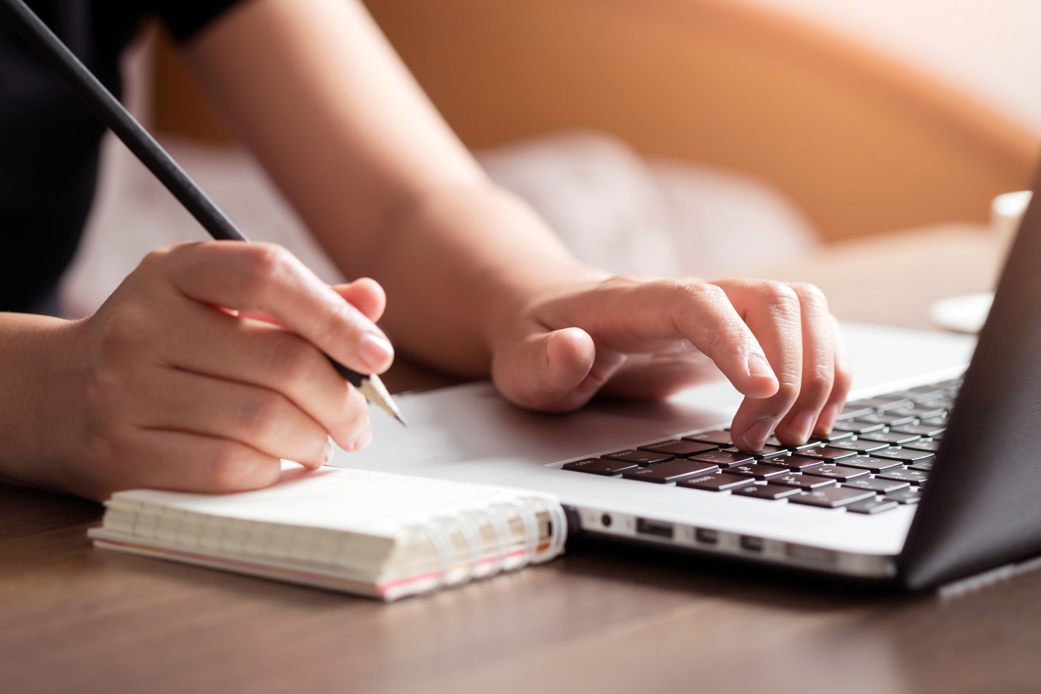 hands writing in notebook and typing on laptop