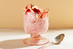 A glass of coconut granita topped with fresh fruit and a spoon beside it