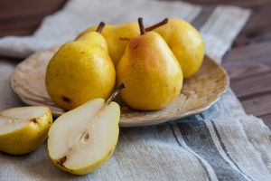 A plate with whole pears and a halved pear on a clothcovered surface