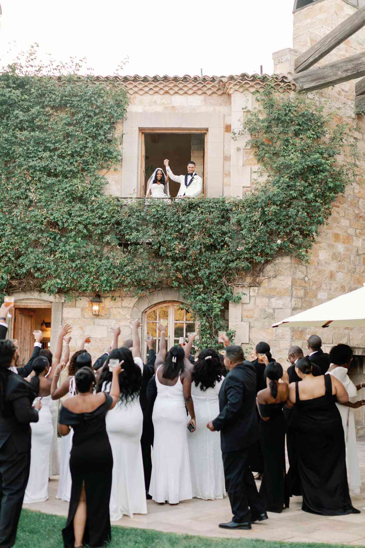 bride and groom toasting to guests below from balcony