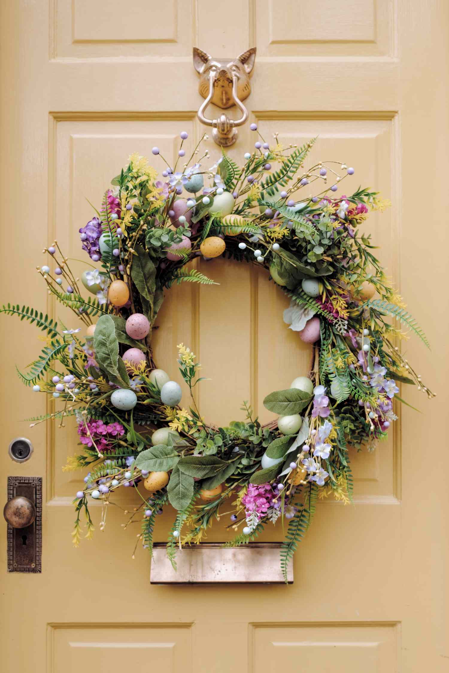 A decorative wreath with flowers and painted eggs hanging on a door