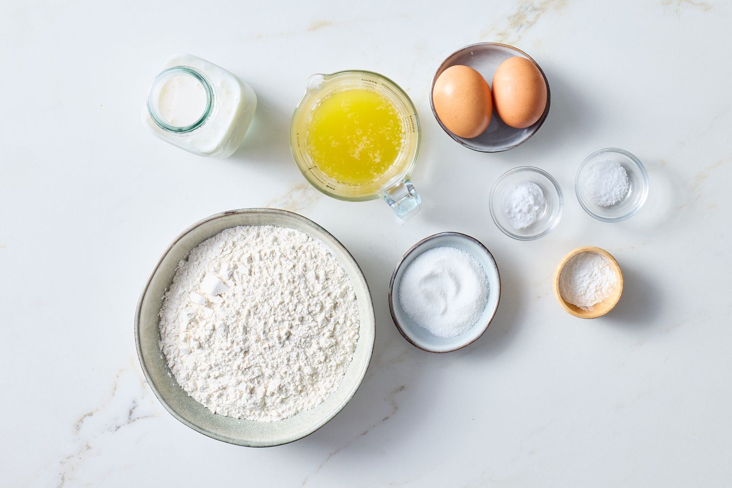 Ingredients for making buttermilk waffles including flour eggs and melted butter placed on a surface