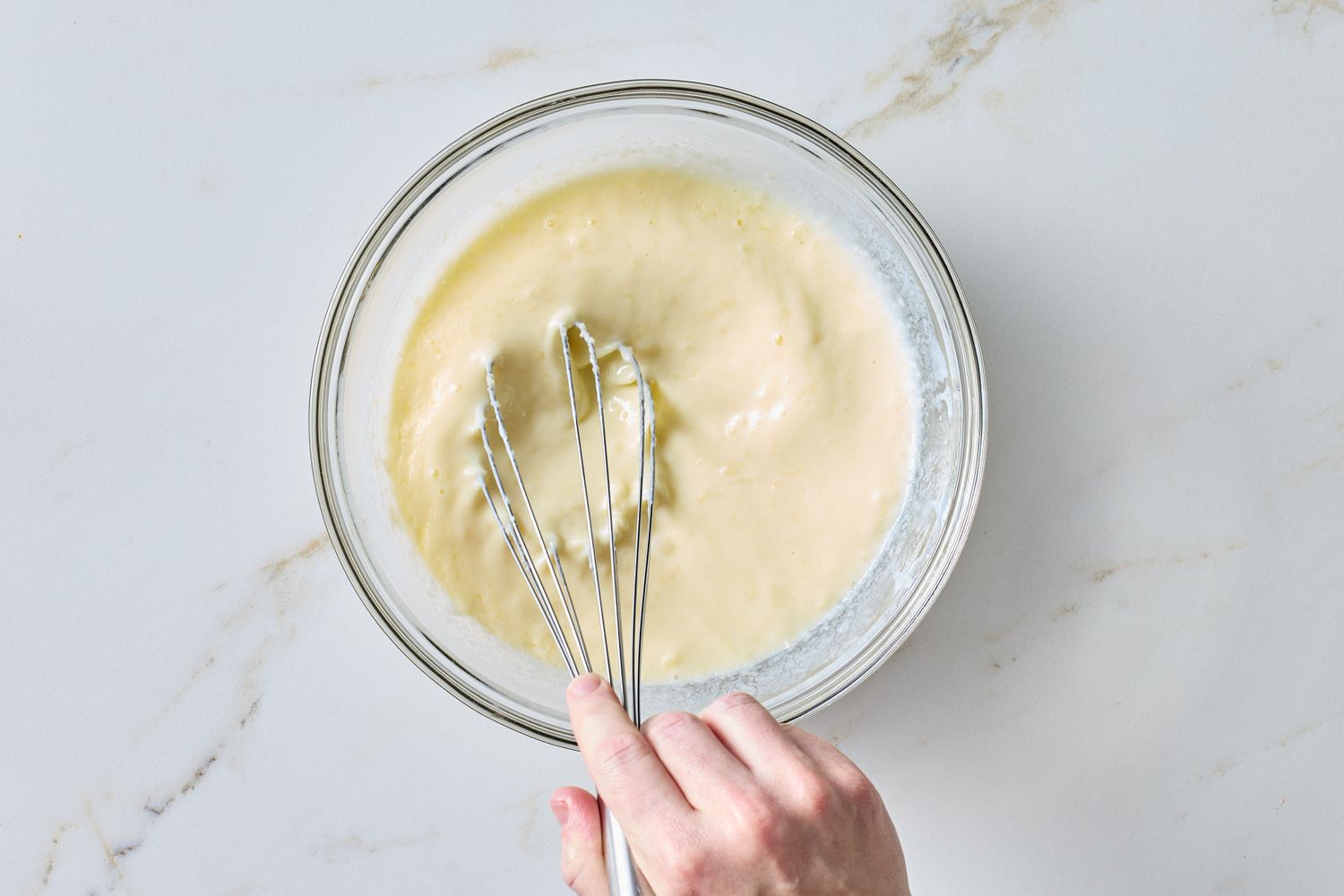 A bowl of batter being mixed with a whisk by a hand
