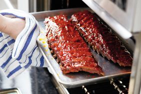 A tray of cooked glazed ribs being taken out of an oven with a towel