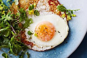 Egg cooked sunny side up served with fresh greens on a plate