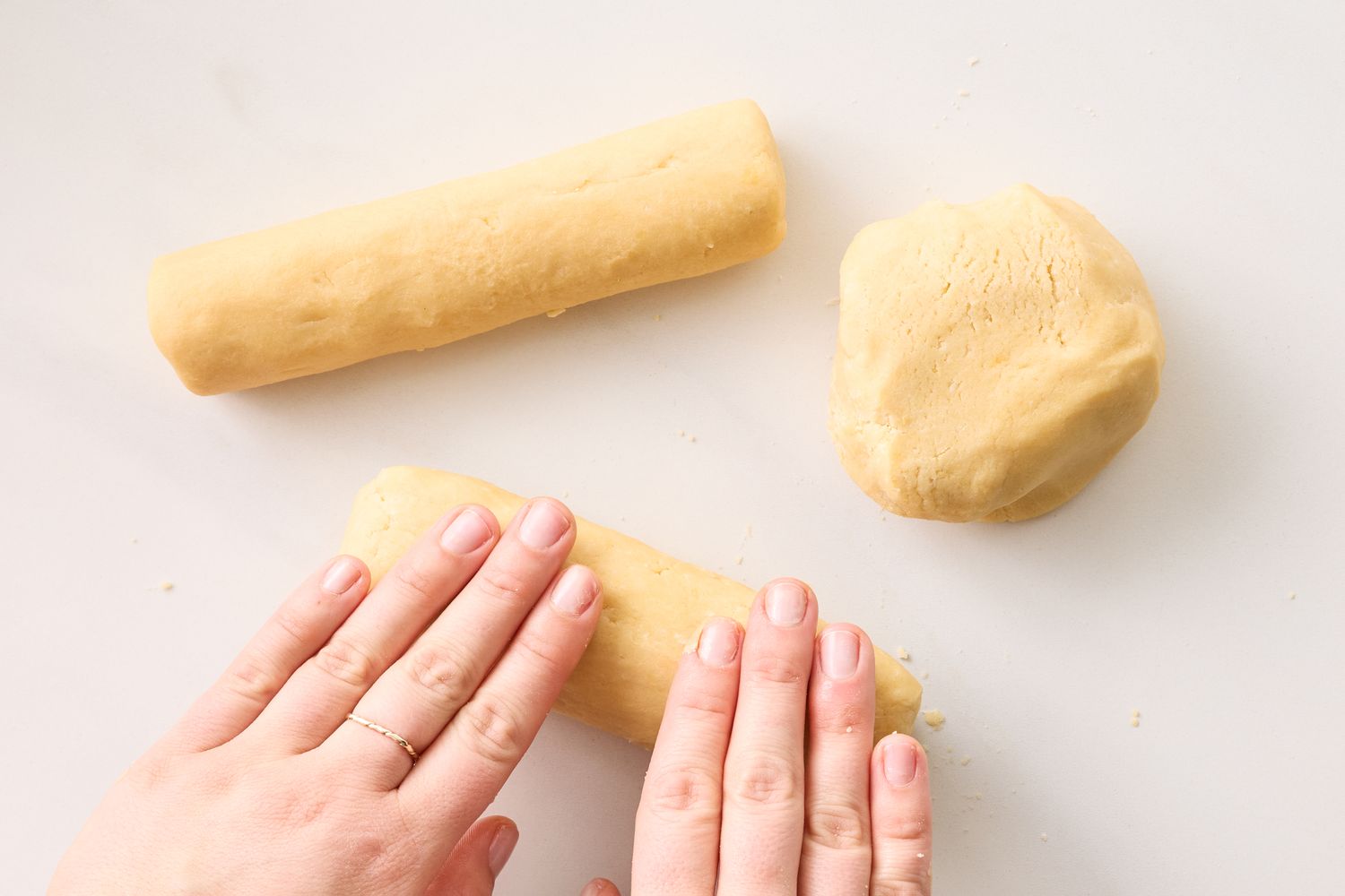 Hands shaping butter cookie dough into logs on a countertop a portion of the dough is set aside as a ball