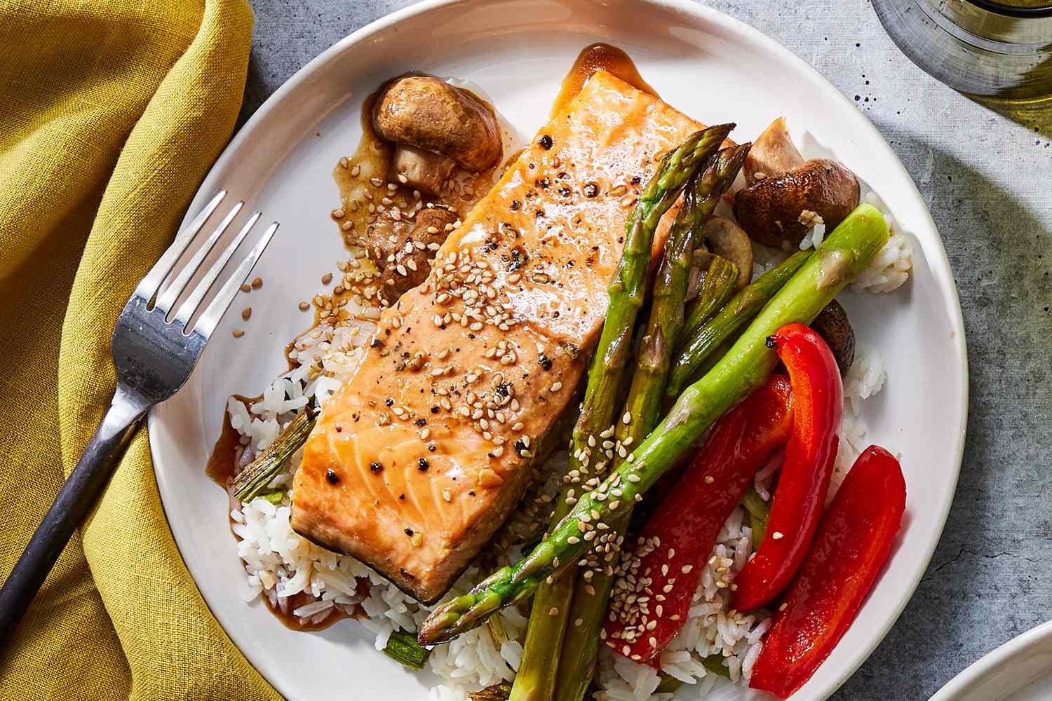 Grilled salmon served on white rice accompanied by roasted asparagus red bell peppers mushrooms and sprinkled with sesame seeds