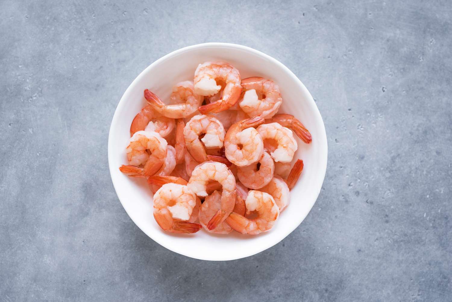 Cooked shrimp arranged in a white bowl on a gray surface